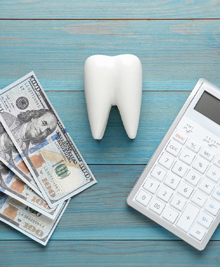 $100 bills next to model tooth and calculator on blue wooden surface