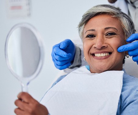 Woman in dental chair smiling holding mirror with dentist touching her cheek