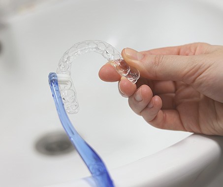 Patient using toothbrush to clean aligners in sink