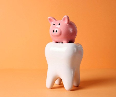 Pink piggy bank sitting on large model tooth with orange background