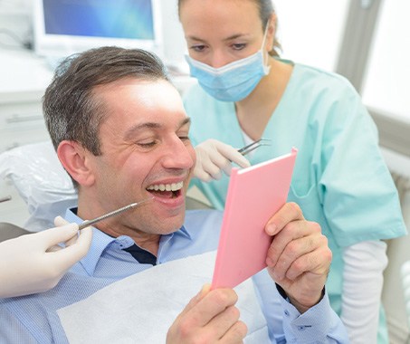 A man looking at his new dental crown in a mirror