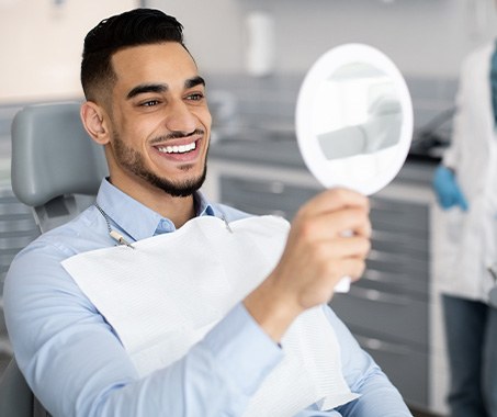 Man smiling at reflection in handheld mirror