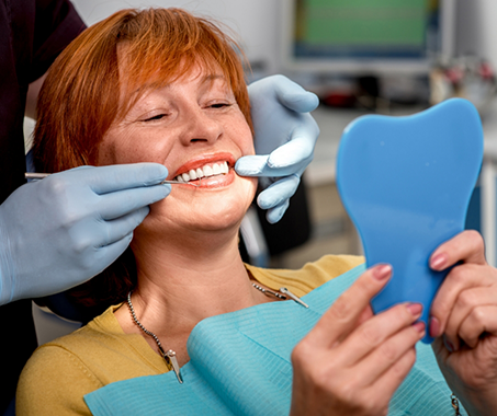 Redheaded dental patient admiring her smile in a mirror