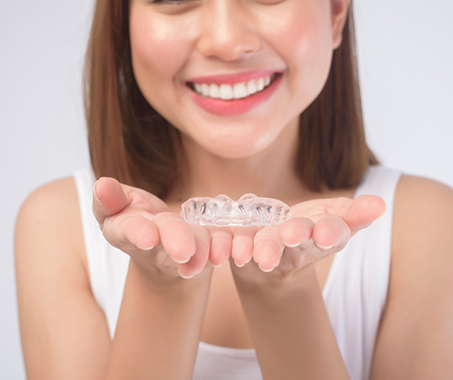 Smiling woman holding an Invisalign aligner in both palms