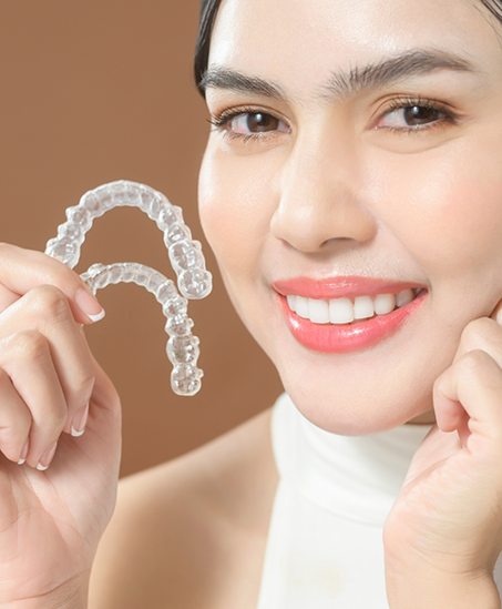 Smiling woman holding two Invisalign trays and touching her face