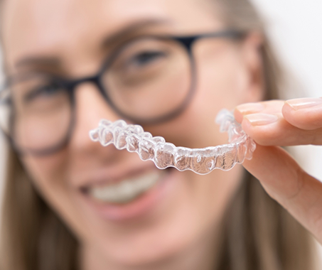 Smiling woman with glasses holding Invisalign