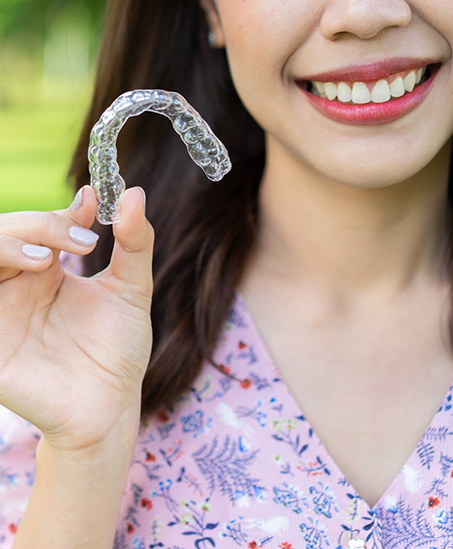 Smiling woman holding an Invisalign aligner