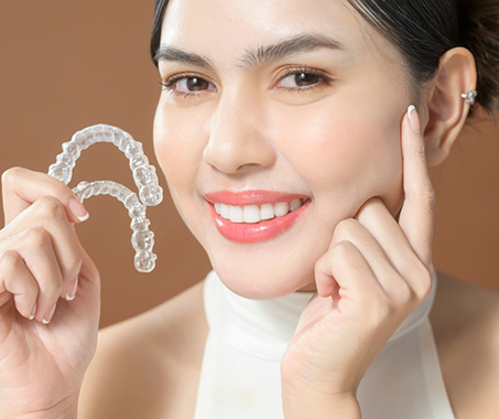 Smiling woman holding two Invisalign trays and touching her face