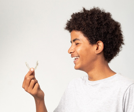 Teenage boy smiling while holding clear aligner