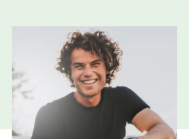 Young man with curly brown hair smiling outdoors