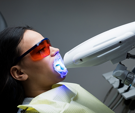 Dental patient getting her teeth whitened by a light